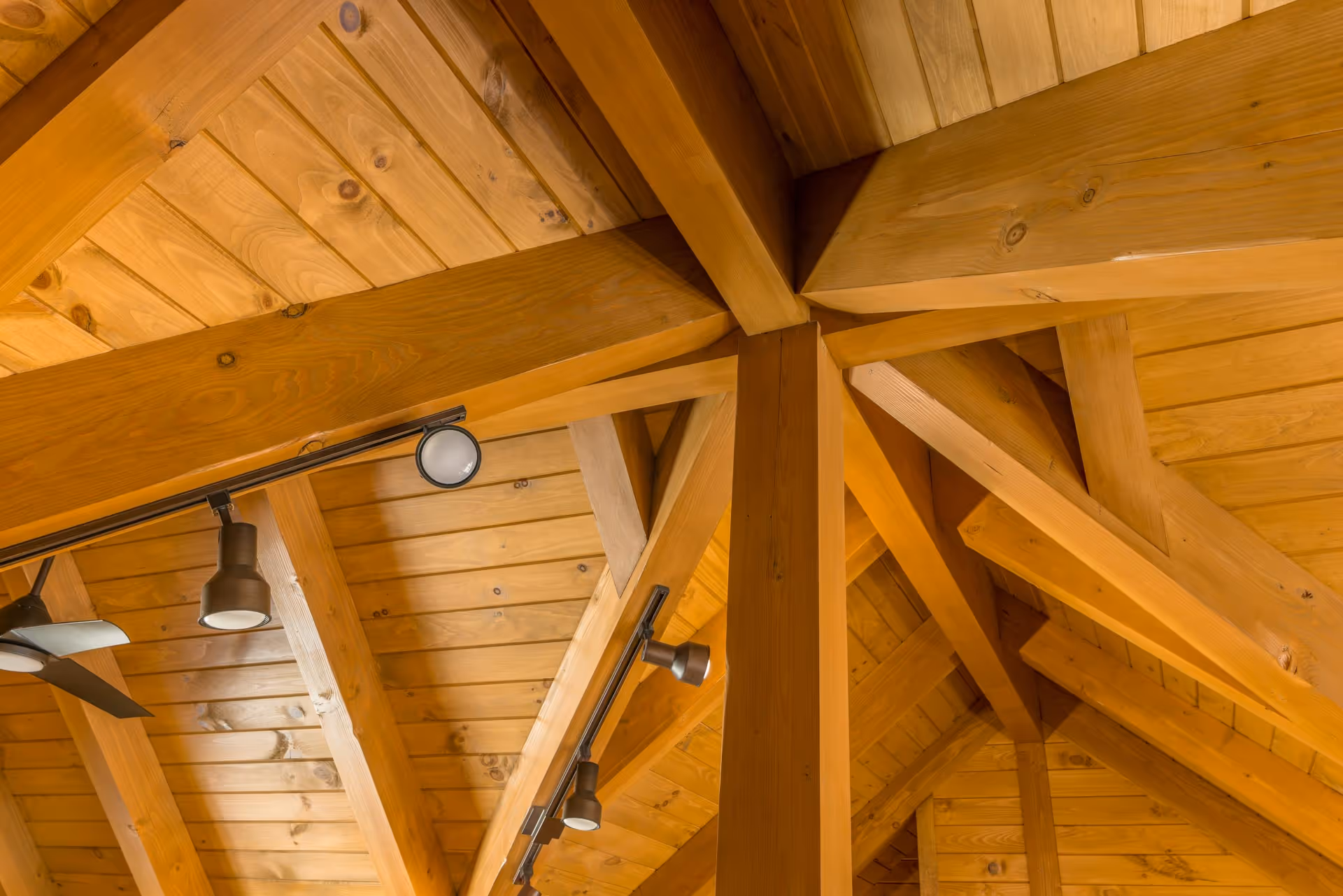 Close-up view of a wooden ceiling with exposed beams and light fixtures, showcasing a rustic design with a warm color palette.