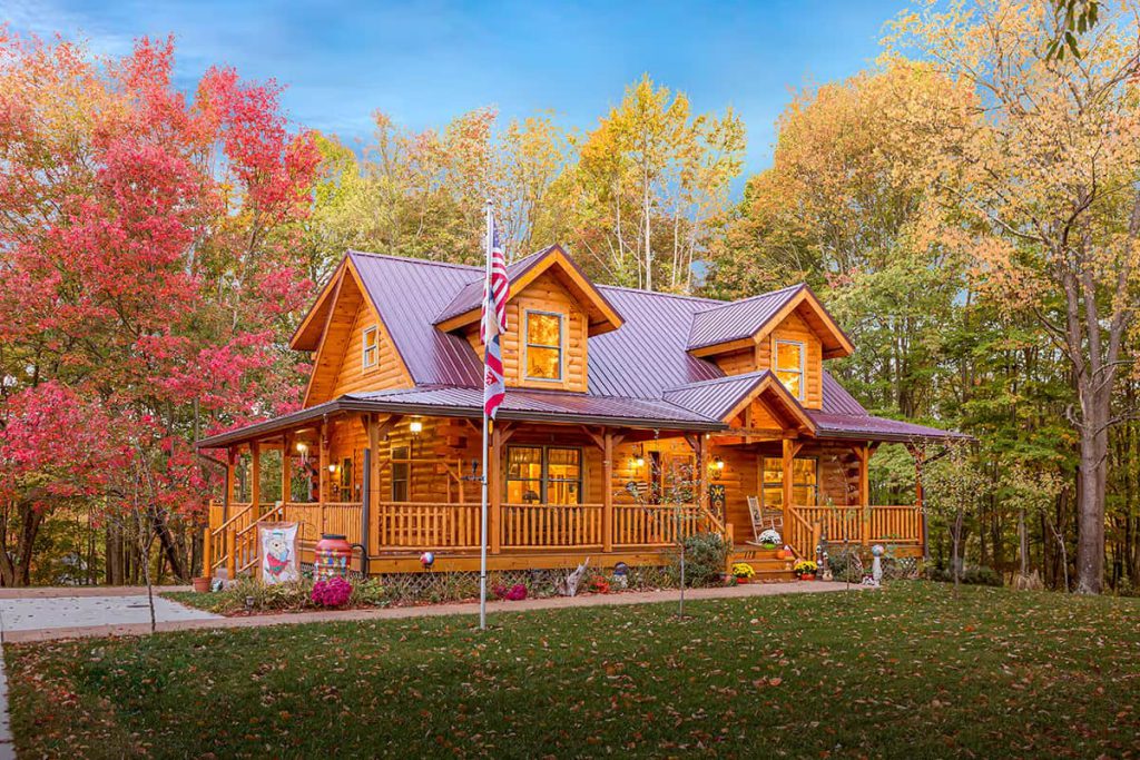 Front exterior of the Pennsylvania Werner Log Home featuring a wraparound porch, dormer windows, metal roof, and fall foliage.