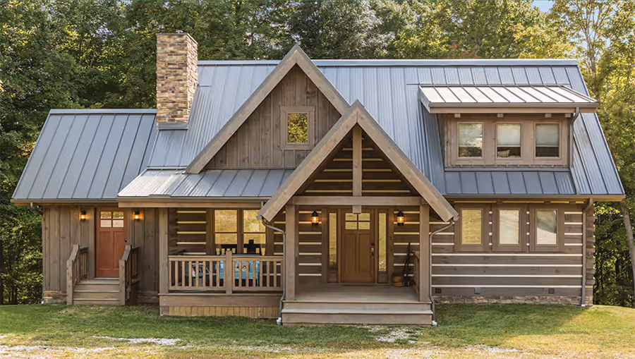 A charming rustic cabin with a metal roof and wooden exterior, featuring a large porch with seating, surrounded by lush greenery. The house displays a mix of modern and traditional architectural elements, inviting and warm atmosphere.