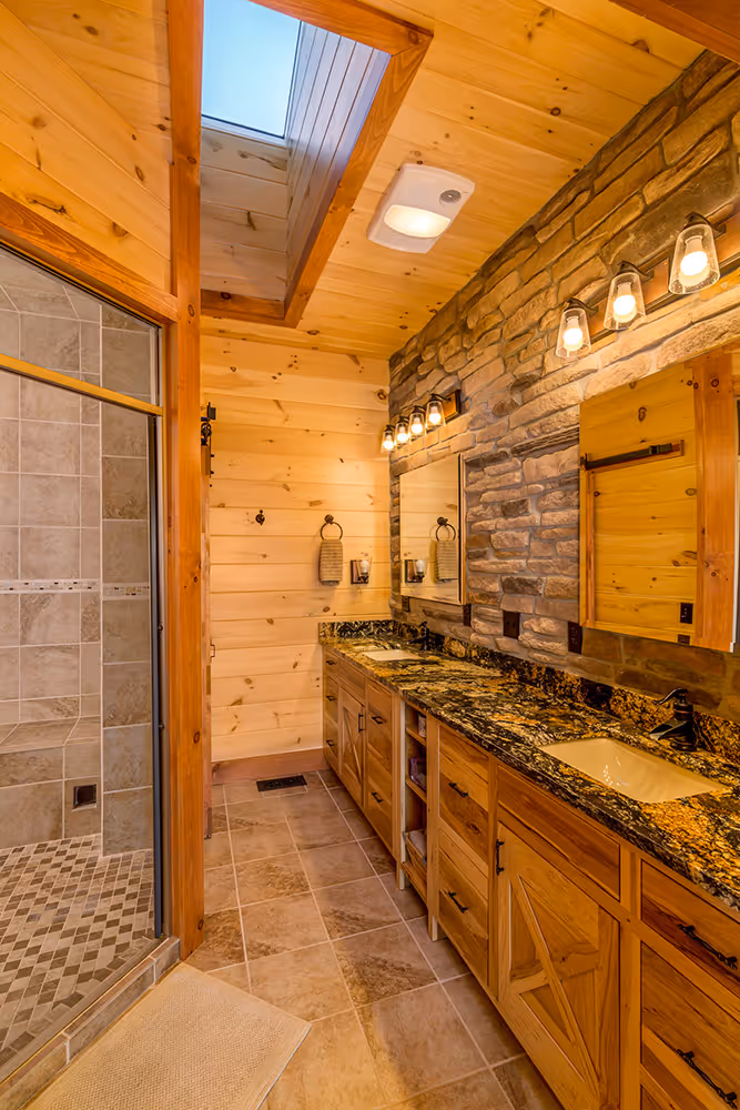 A modern bathroom featuring wooden paneling and a stone accent wall. The space includes a double vanity with granite countertops, a large mirror, and two sconces.
