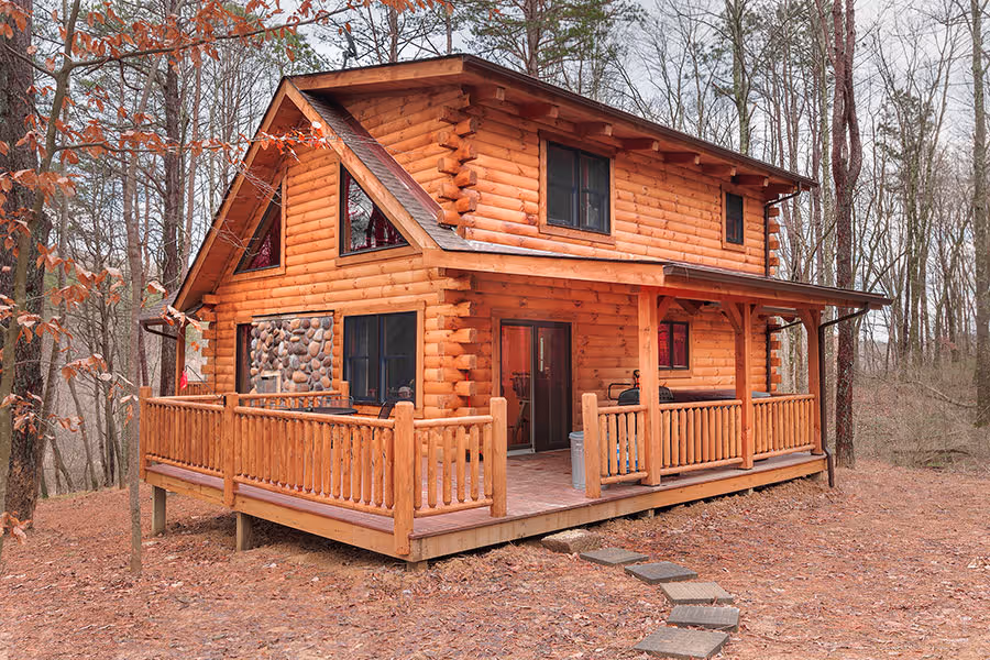 Bell Log Home in Hocking Hills, Ohio, featuring a two-story log cabin design, covered wraparound porch, stone accents, and wooded surroundings.