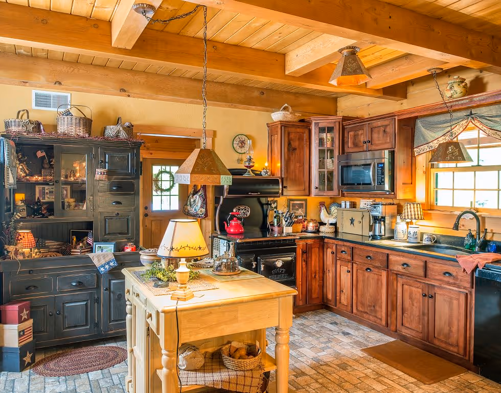 A warm and inviting rustic kitchen featuring wooden beams, rich brown cabinets, and a stylish black oven. A small island with a lamp sits in the center, surrounded by decor and a window letting in natural light.