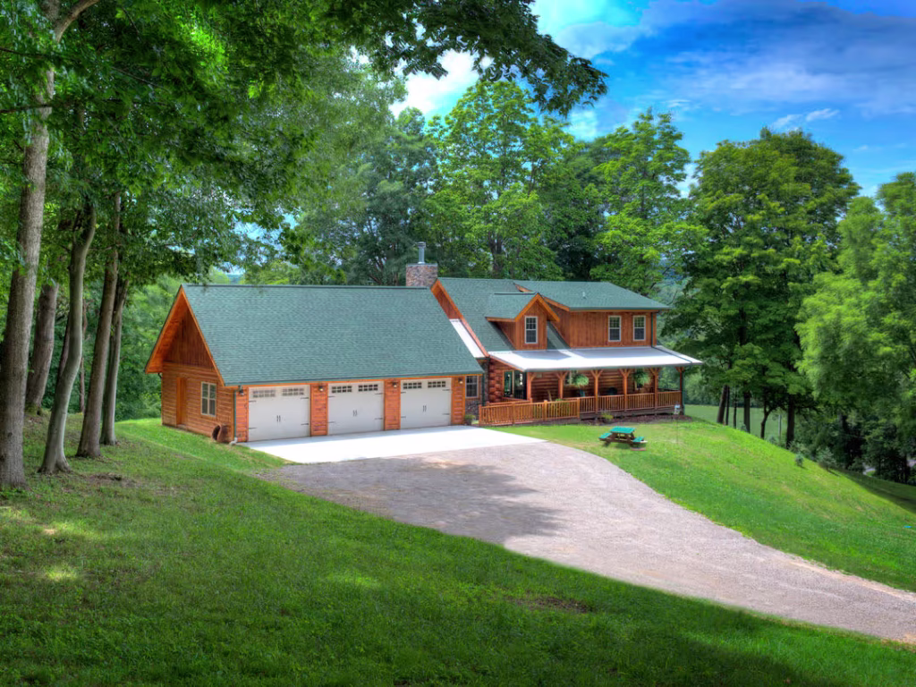 A beautiful wooden house with a green roof, surrounded by lush trees and a sloping lawn. A gravel driveway leads to the home, enhancing its charming, rustic appeal. Natural sunlight illuminates the scene, creating a serene atmosphere.