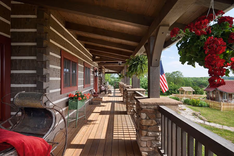A cozy wooden cabin nestled among vibrant autumn trees, featuring a spacious deck with railings and steps leading to the ground. The cabin’s warm wood tones contrast beautifully with the colorful foliage.
