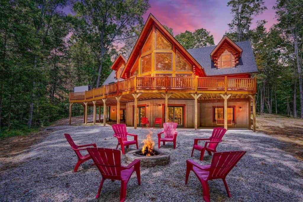 Beautiful log home with large deck and outdoor fire pit at sunset.