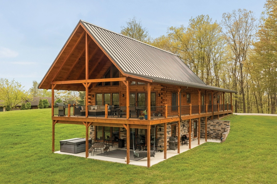 Chalet log home exterior by Hochstetler Log Homes featuring a covered deck, timber frame design, and expansive windows.