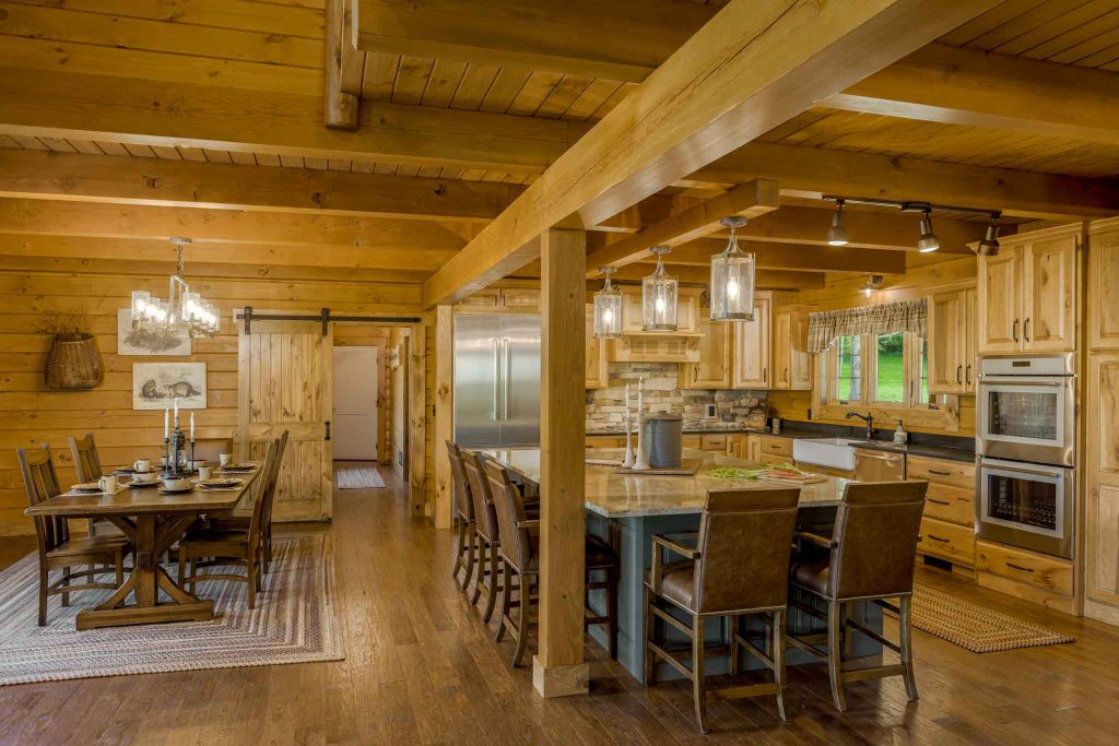 A spacious rustic kitchen and dining area featuring wooden beams and cabinetry, with a large island and barstool seating. A dining table is set nearby, enhancing the warm, inviting atmosphere of the home.