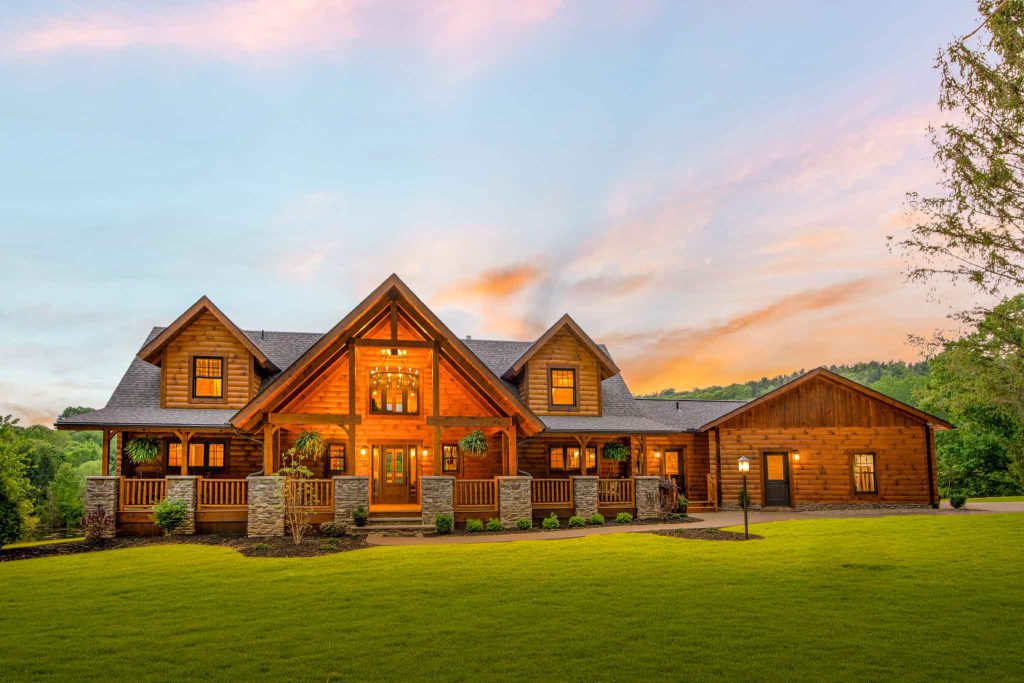 A charming wooden cabin with large windows, nestled on a grassy slope next to a serene lake. Surrounding trees reflect in the water, creating a peaceful, natural setting, with a small fire pit visible in the foreground.