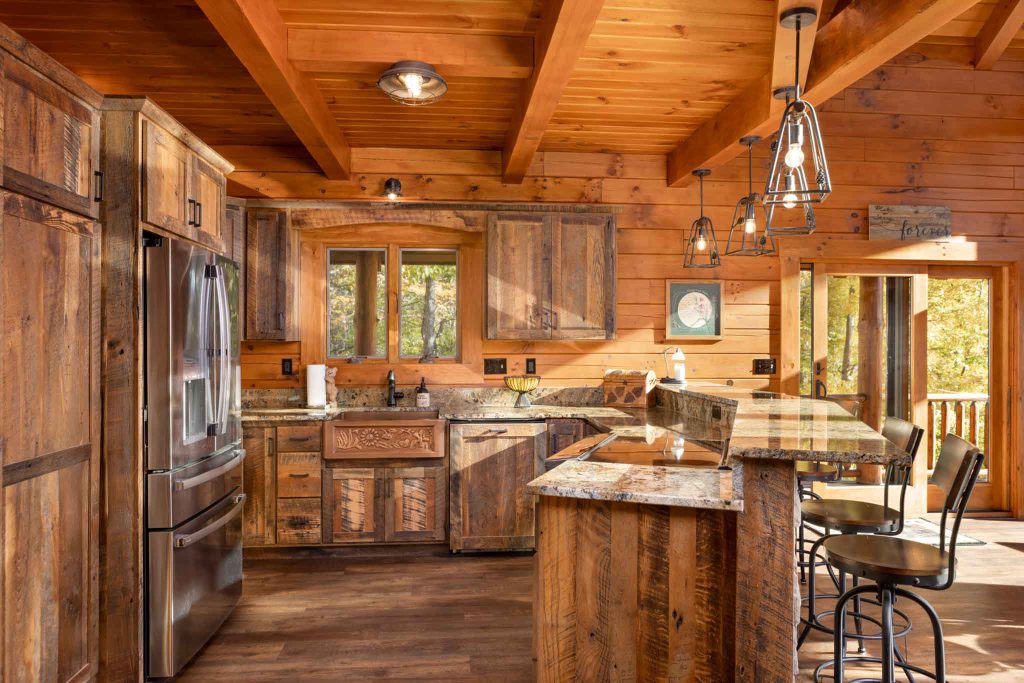 A rustic kitchen featuring warm wooden cabinets and a granite countertop, with stainless steel appliances and cheerful natural light streaming through large windows. Bar stools are positioned at a kitchen island, creating a cozy atmosphere.