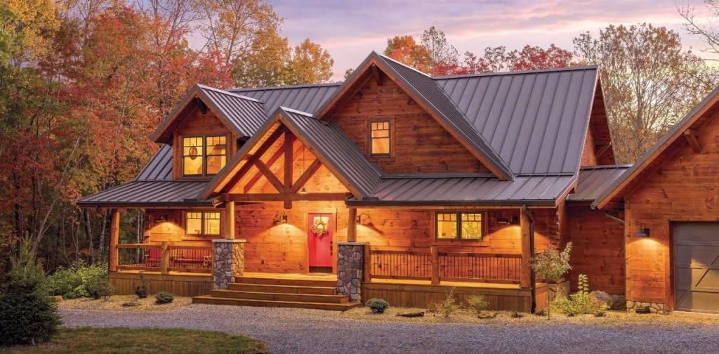 Allison log home by Hochstetler Log Homes at dusk, with wood siding, a metal gable roof, covered porch, stone columns, and attached garage.