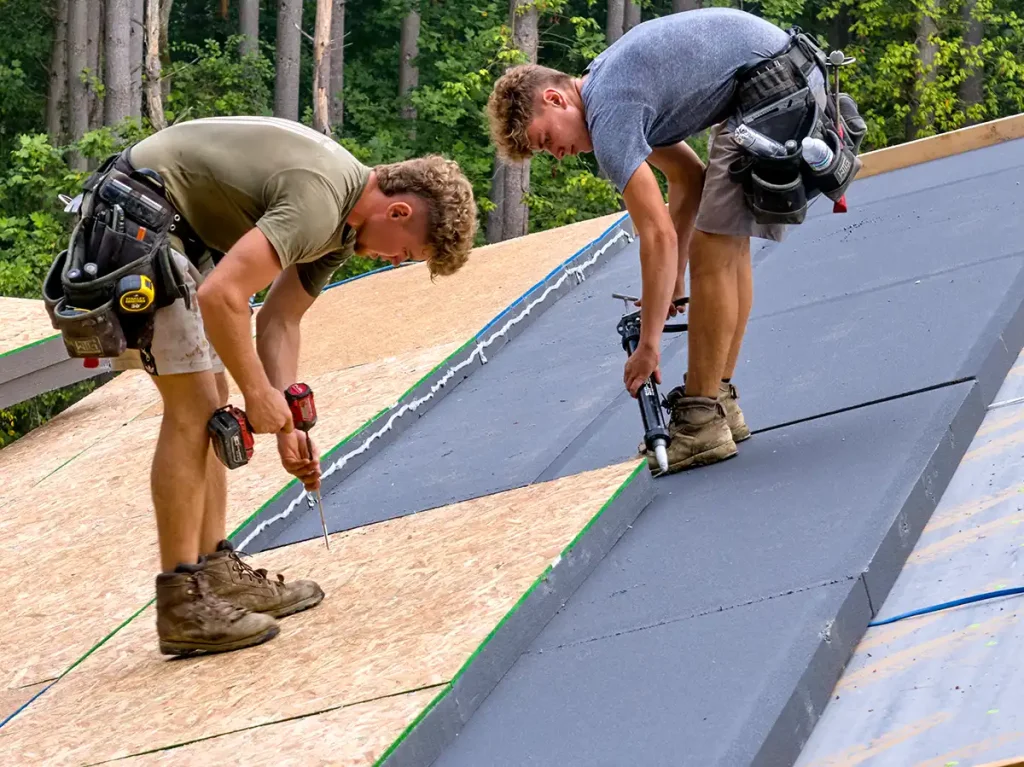 Construction crew installing and sealing insulated roof panels for a Hochstetler log home timber roof system.