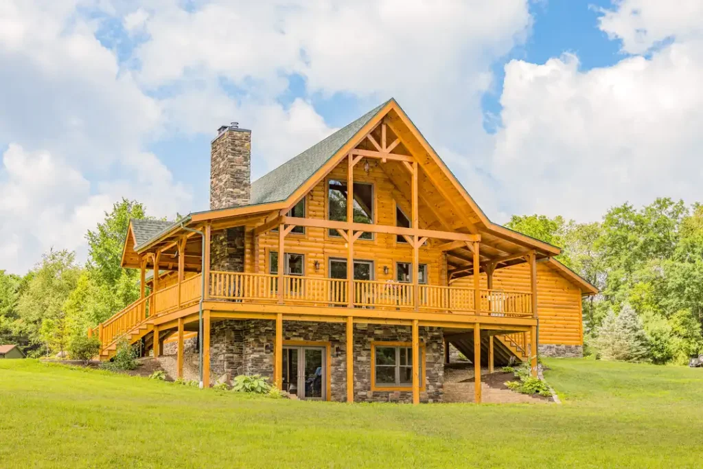 Hochstetler log home exterior with a timbered glass gable, stone chimney and foundation, and spacious wraparound deck.