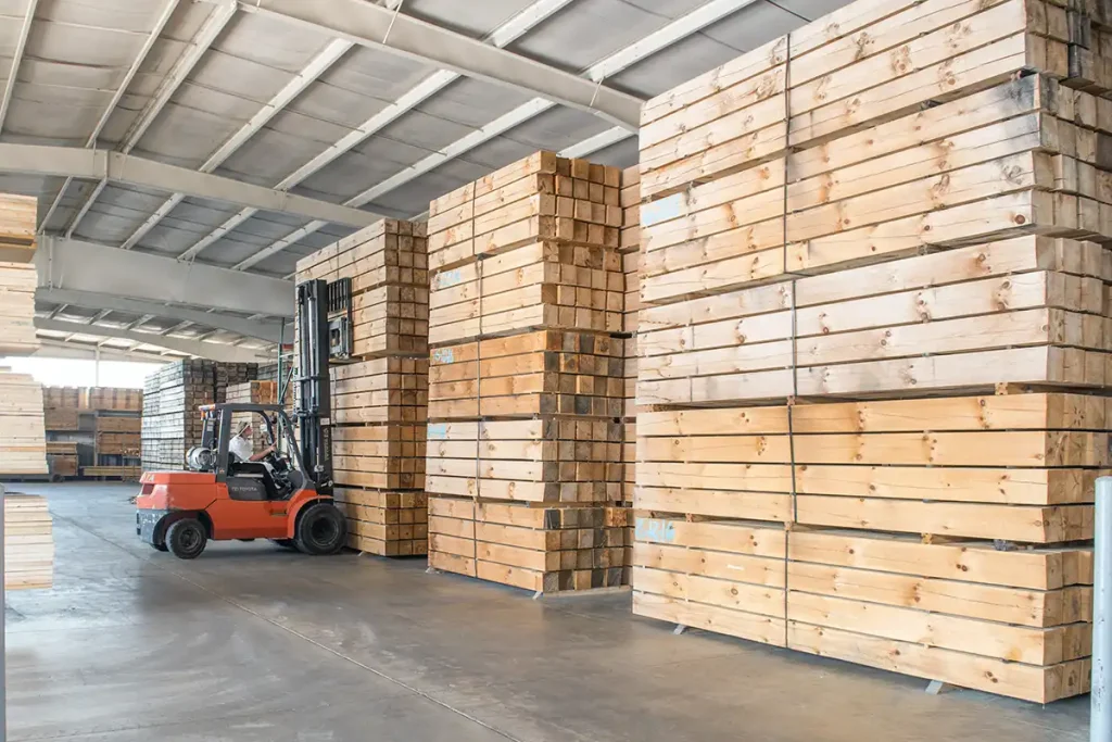 Stacks of American-sourced dried timbers stored at Hochstetler Log Homes, with a forklift moving lumber inside the production facility.