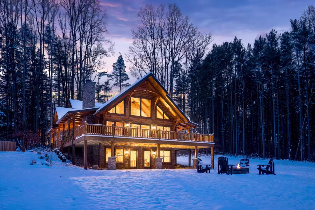 Hochstetler Log Home exterior in Ohio at dusk with gable-window great room and wraparound deck in snowy woods
