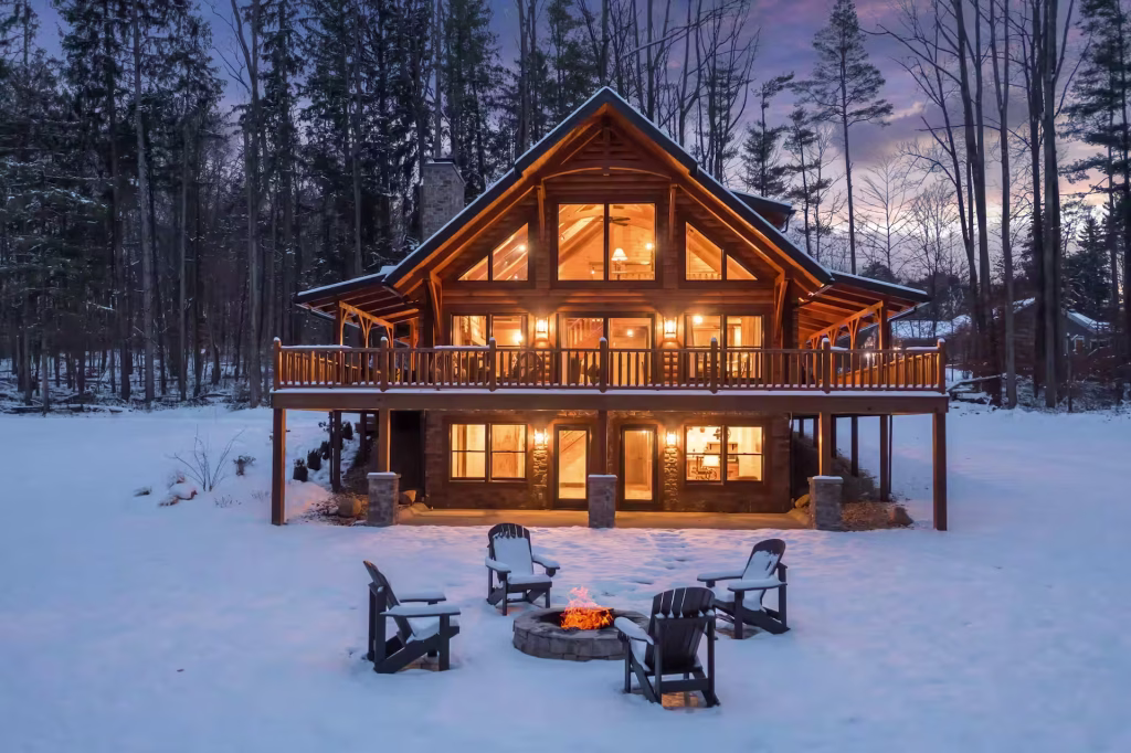 Rear view of the Hochstetler Log Home with full-height gable glass, upper deck, and walkout lower level by a fire pit
