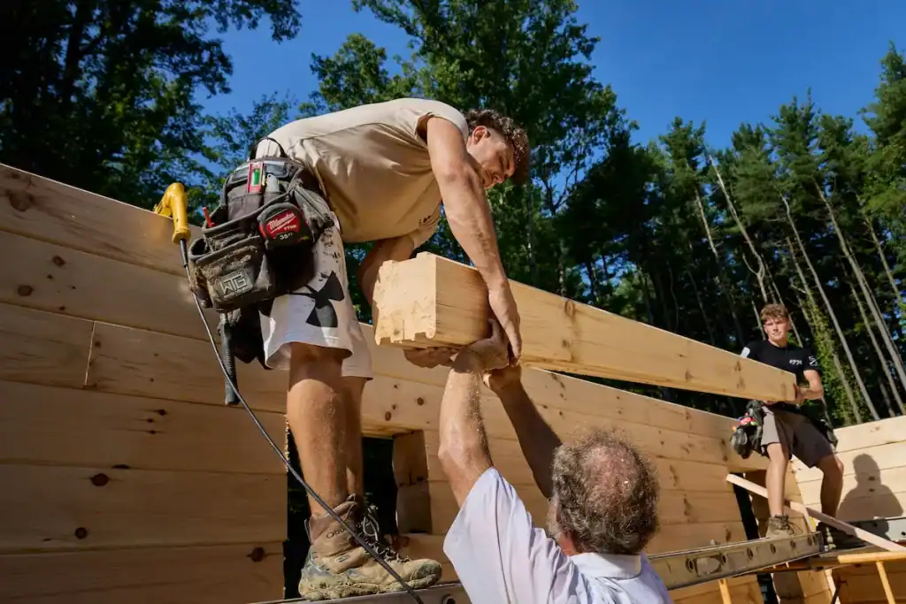 Workers building a log home with timber and tools on site.