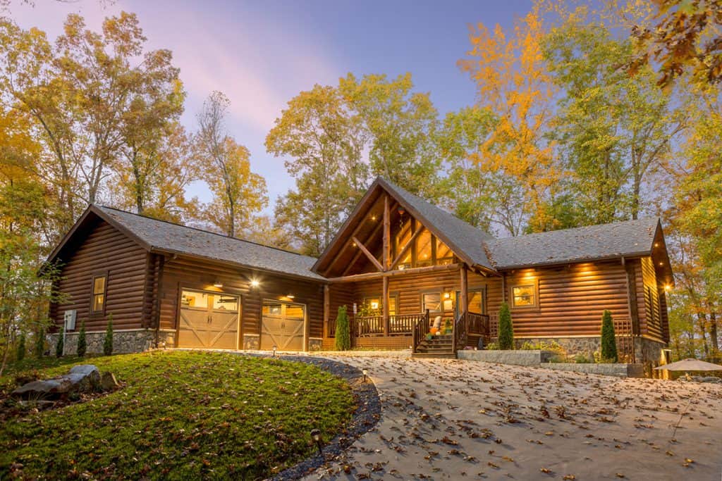 Beautiful log home with warm lighting in a wooded setting at dusk.