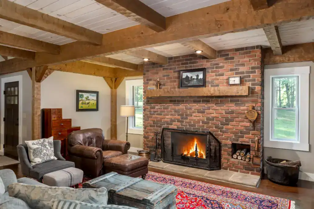 Living room in Stacy and Dave’s historic-inspired log home with exposed timber beams, brick fireplace and traditional furnishings.