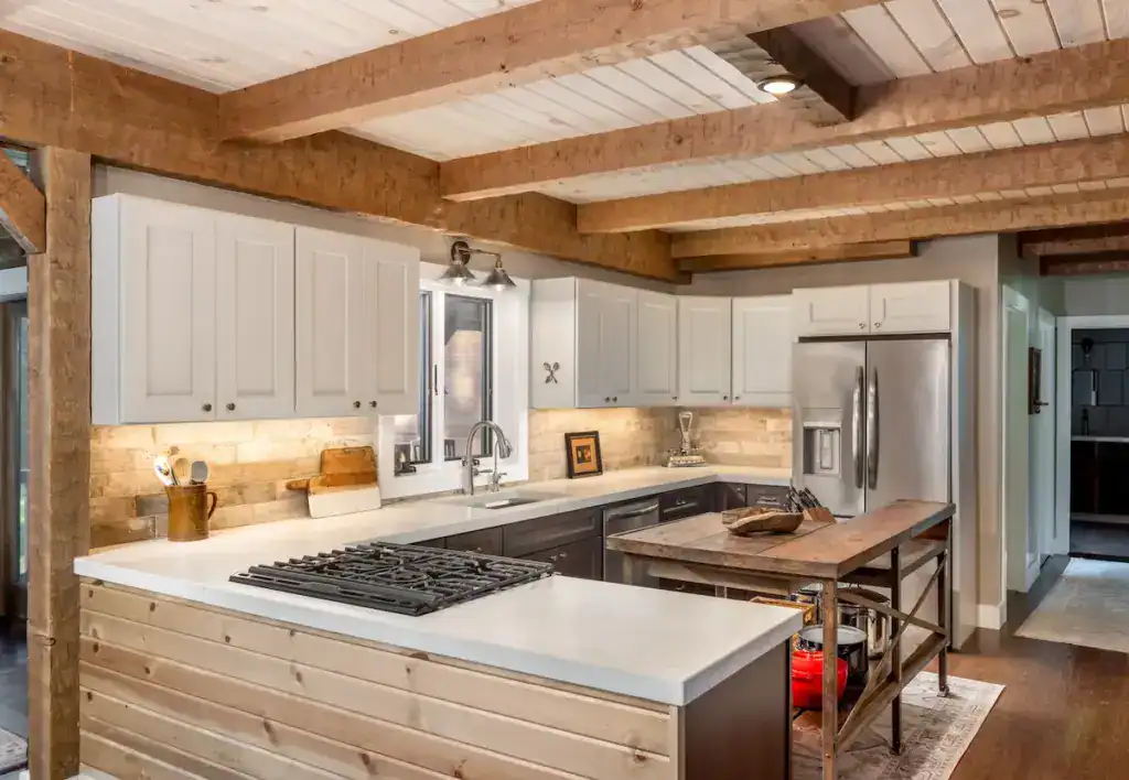 Kitchen in Stacy and Dave’s historic-inspired log home with exposed timber beams, light cabinetry and concrete countertops.