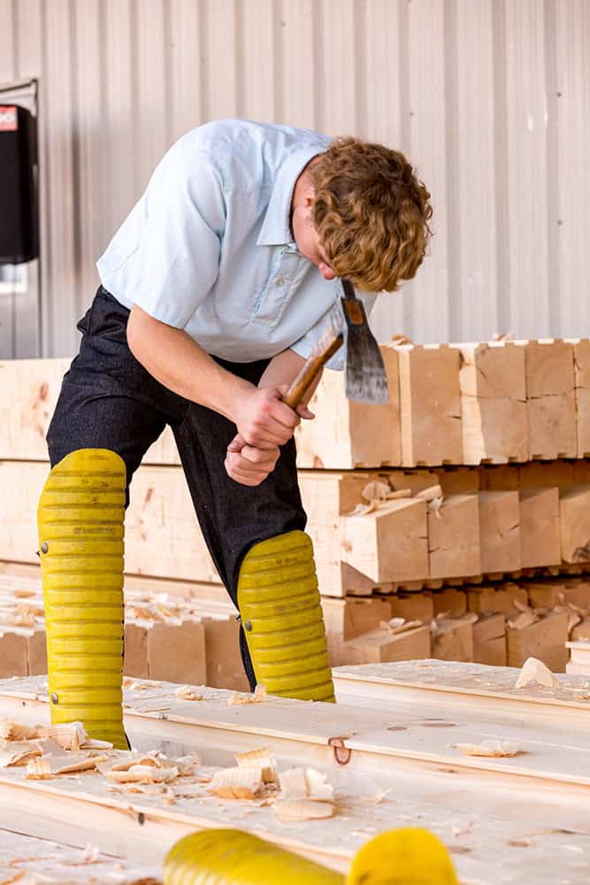Carpenter shaping wood with axe in a woodworking shop.