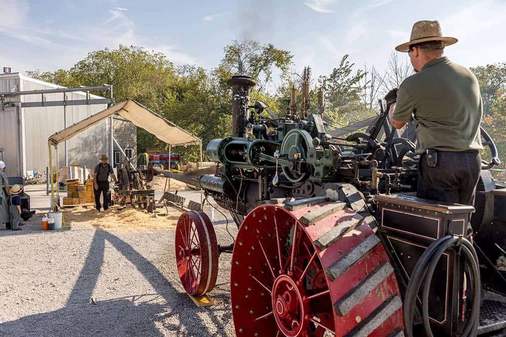 Man operating a vintage steam tractor at Log Cabin Days event.