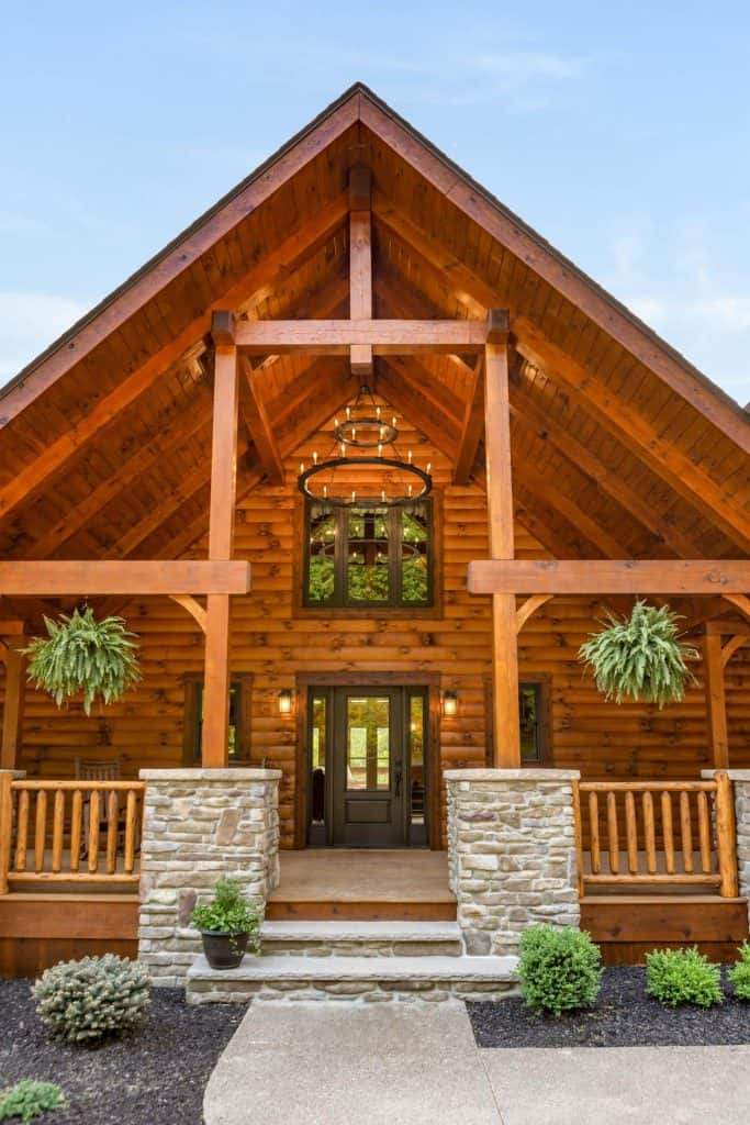 Front view of a Hochstetler Log Homes cabin with stone steps and hanging plants.