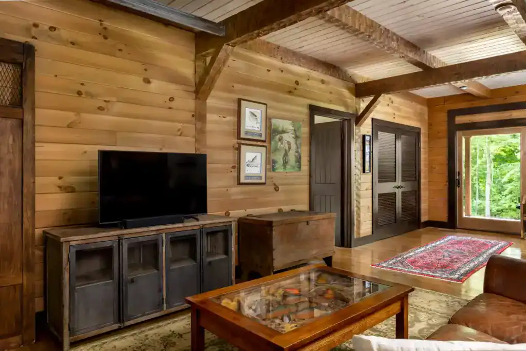 Living area with knotty pine plank walls, exposed timber beams, a rustic media cabinet and a glass-top display coffee table