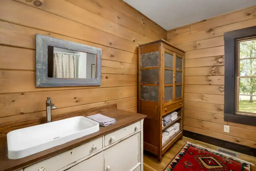 Bathroom with pine plank walls, a vessel sink on a painted wood vanity, a rustic framed mirror and an antique pie safe