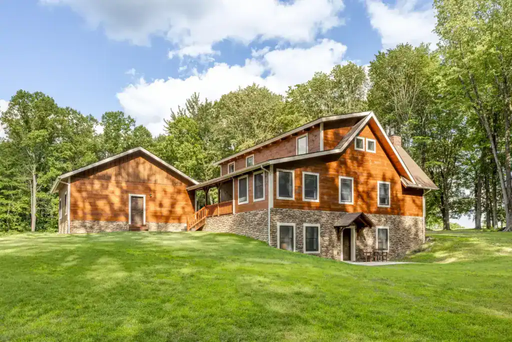 Rear view of a two-story wood-sided home with a fieldstone walkout lower level, covered porch and attached garage on a green lawn