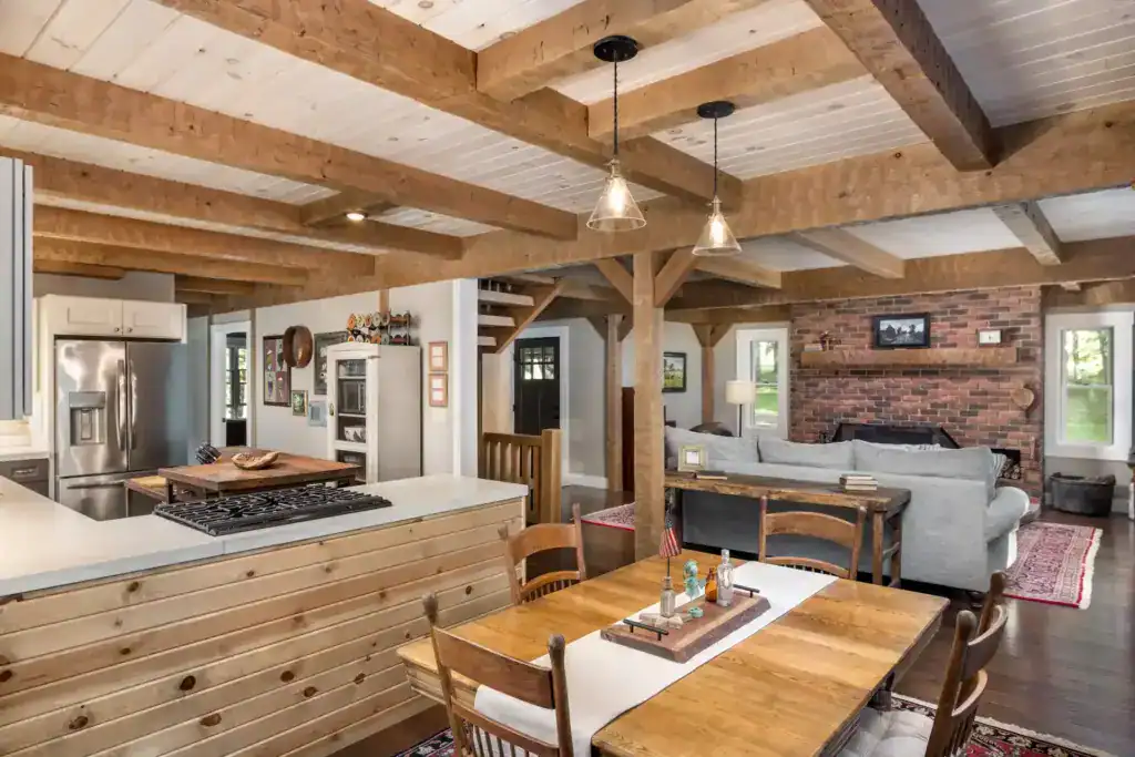 Open kitchen, dining and living area with exposed timber beams, pendant lights and a brick fireplace