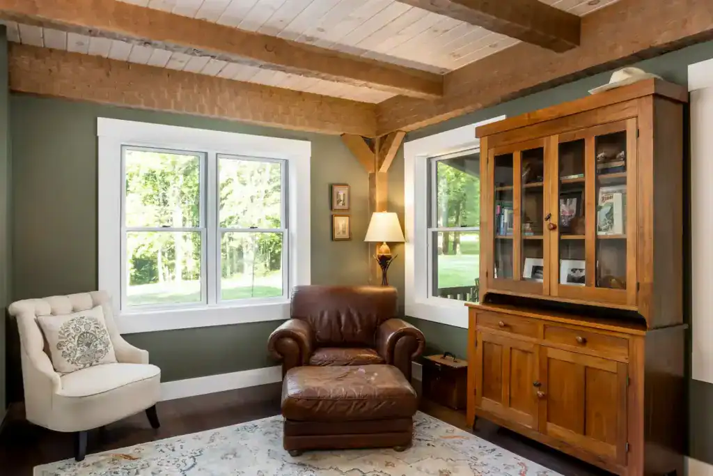 Sitting room with green walls, exposed beams, a leather armchair and ottoman, and an antique glass-front cupboard