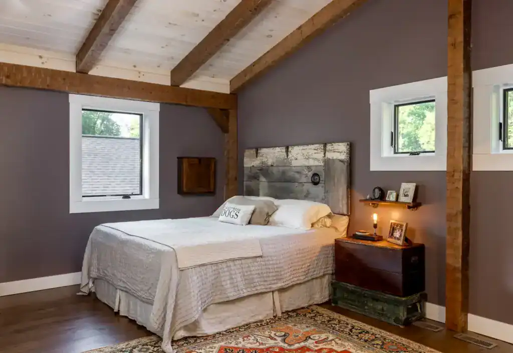 Bedroom with exposed timber beams, a vaulted plank ceiling, a reclaimed-wood headboard and a vintage trunk nightstand