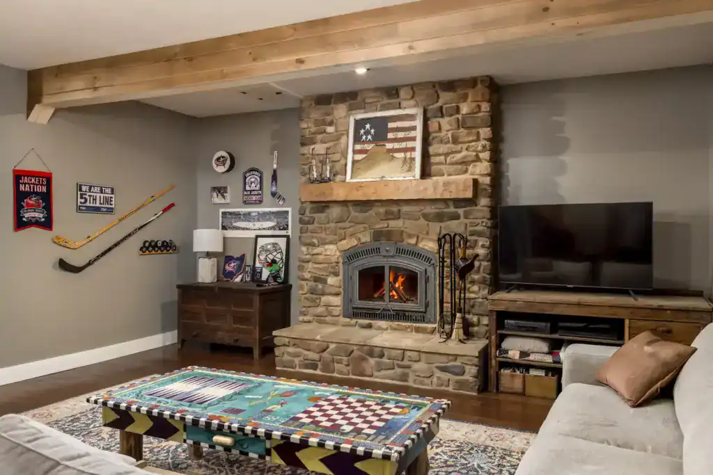 Finished lower level with a stone wood-burning fireplace, timber mantel and beam, hockey memorabilia and a painted game table