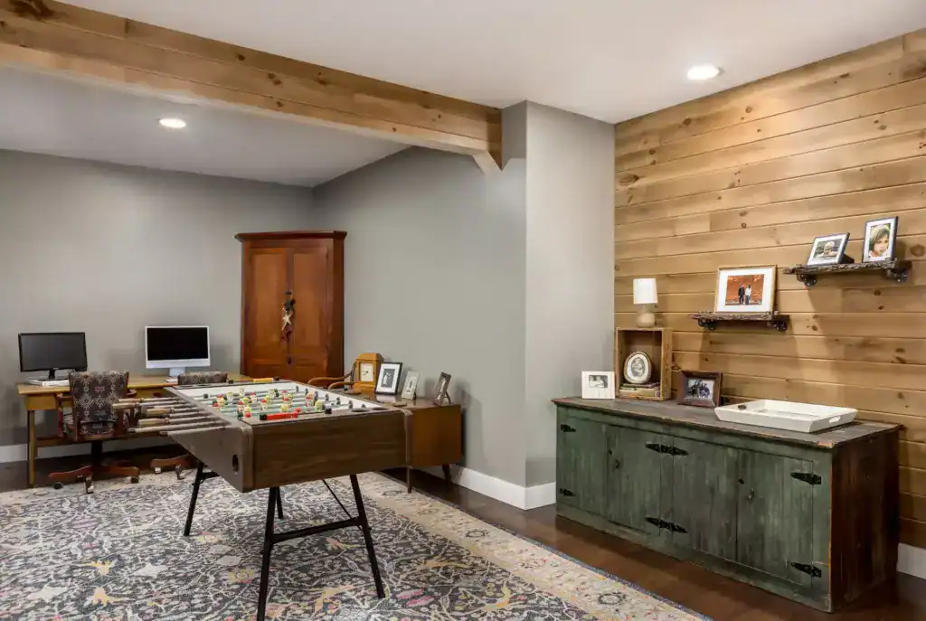 Lower-level game room and office with a foosball table, a wood plank accent wall and an antique green cupboard